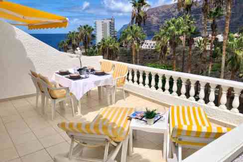 Balcony with outdoor dining setup overlooking Los Gigantes cliffs and ocean.