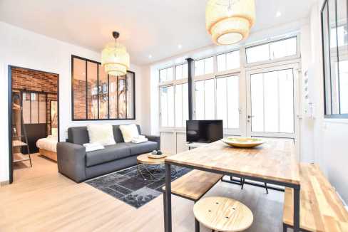 Bright living room with large windows, sofa, and dining area in a serviced apartment.