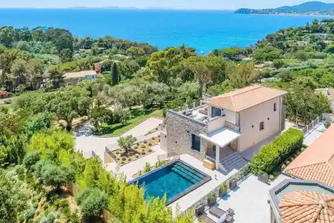 Aerial view of a luxury villa with pool overlooking the sea and lush greenery.