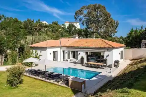 Luxury villa with pool and outdoor lounge in a lush green setting.