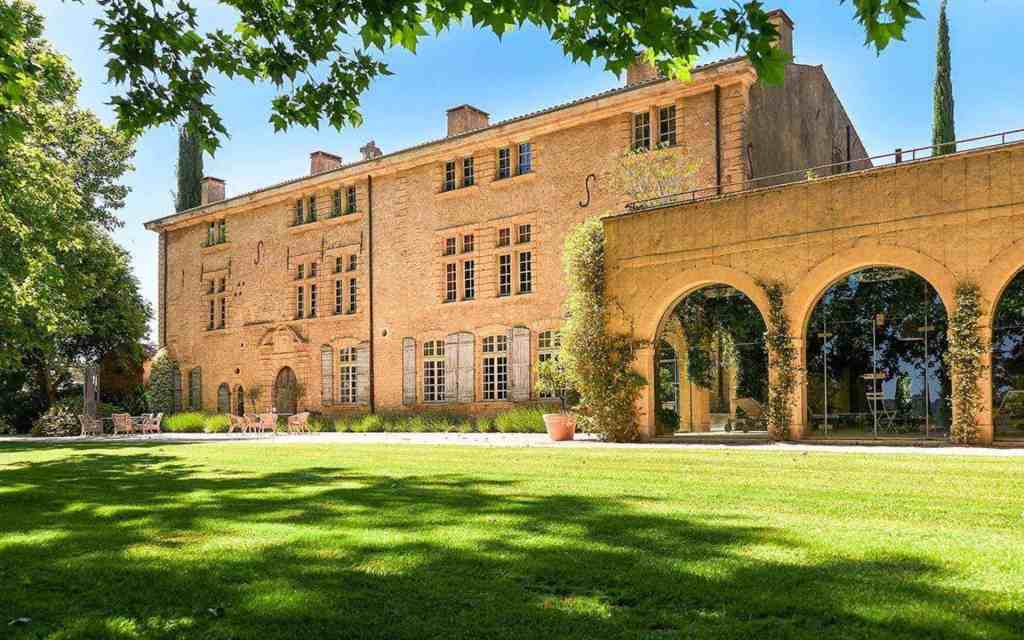 Historic Provençal chateau with lush gardens and arches in the countryside.