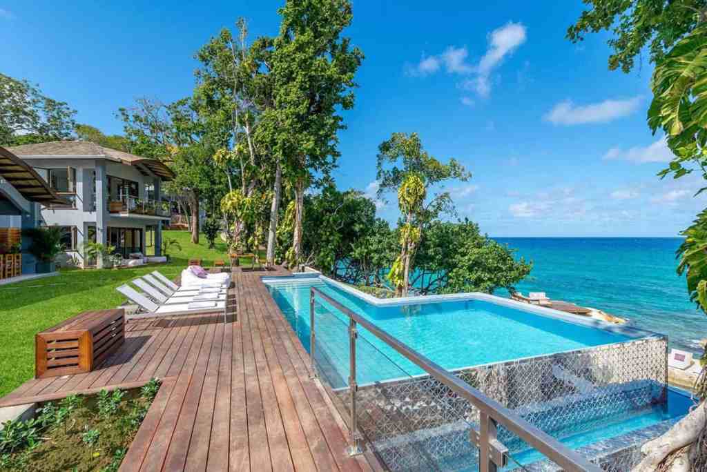Elegant infinity pool overlooking the ocean with lush greenery and modern villa in the background.