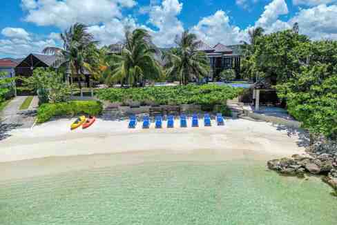 Luxury beachfront villa with palm trees and clear water in Runaway Bay.