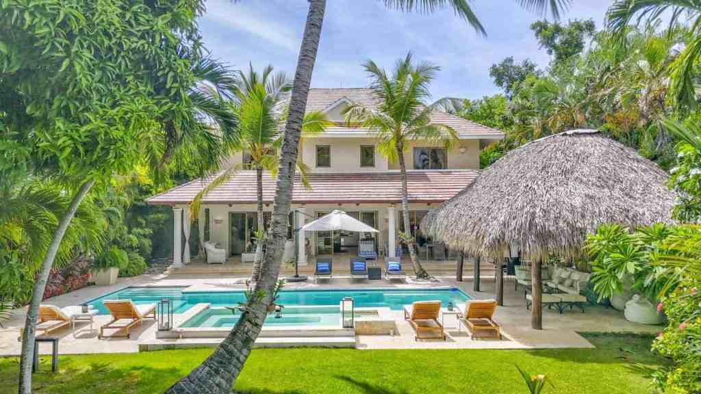 Luxury tropical villa with pool, palm trees, and thatched roof hut.