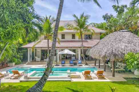 Luxury tropical villa with pool, palm trees, and thatched roof hut.